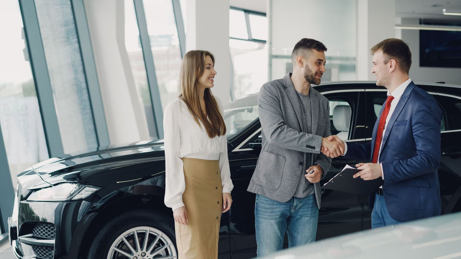 Buyer and seller shaking hands in front of a vehicle at a dealership